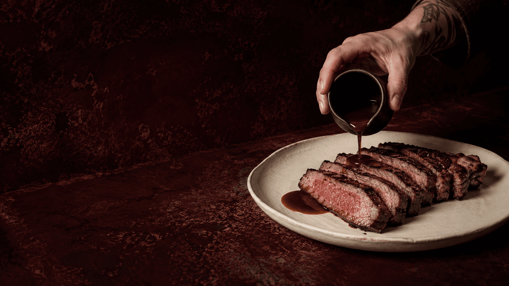 Entrecot al fuego con jugo de cebolla, servido con la mano acercando el plato